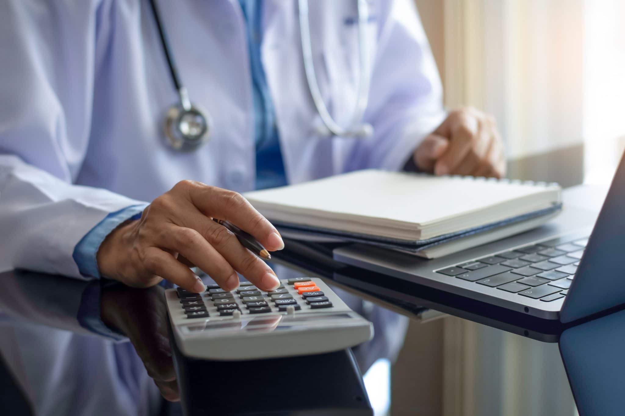 A doctor typing figures into a calculator whilst wearing a stethoscope around her neck