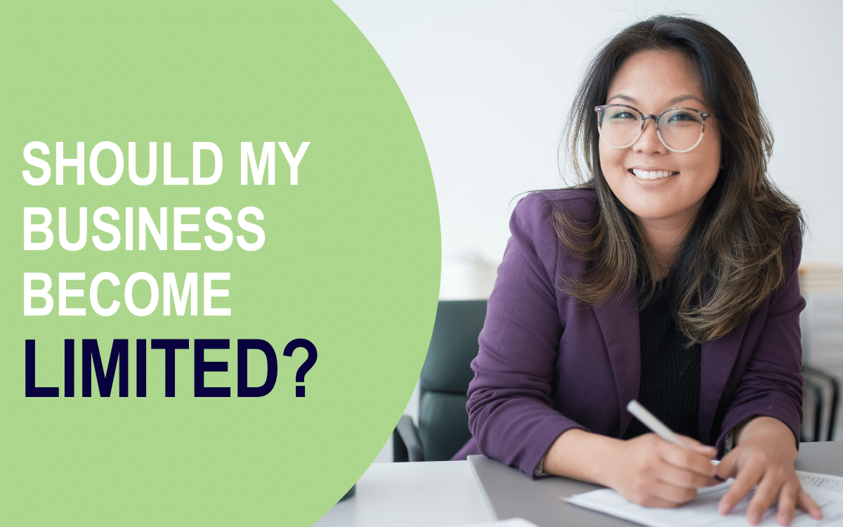 A smiling businesswoman sits at a desk, holding a pen to paper