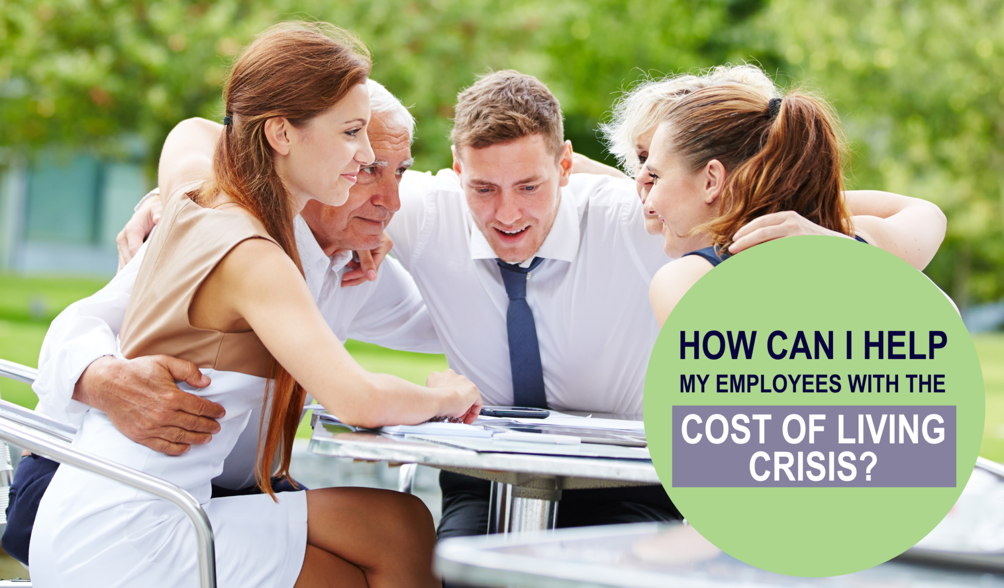 A group of work colleagues in business attire hugging and smiling around a table