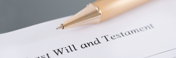 a golden ball-point pen rests on a document entitled 'last will and testament'