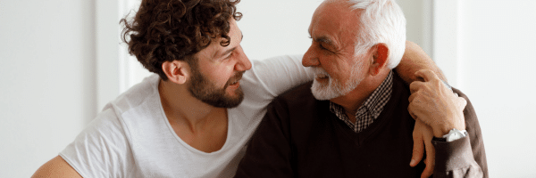 a young man embraces an older man and they smile at each other